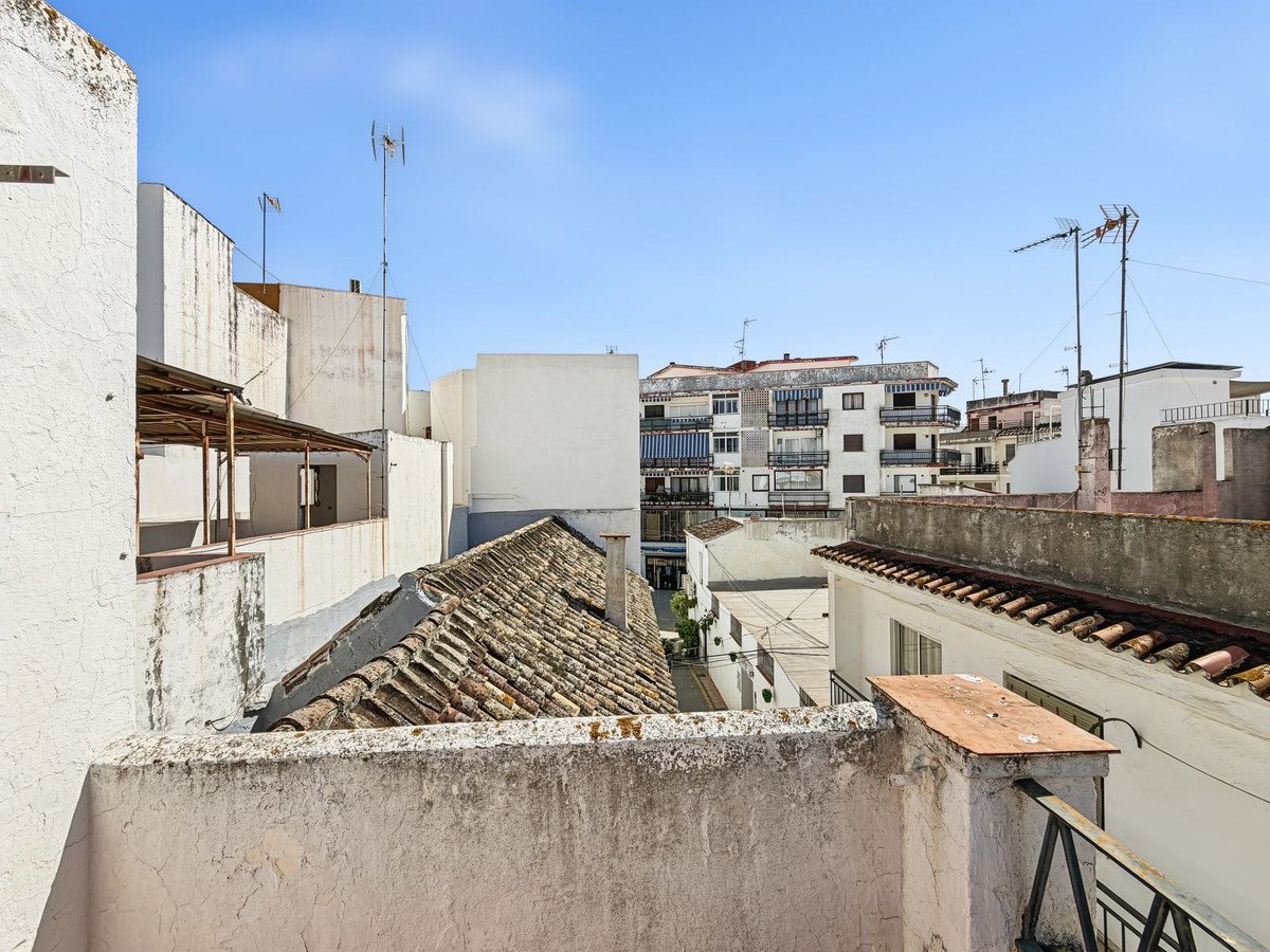 Rooftop view of urban buildings with antennas against a clear blue sky. Some balconies and tiled roofs are visible.