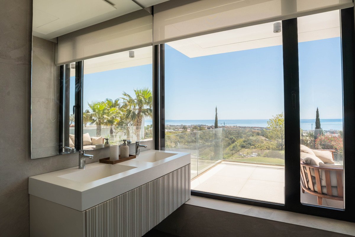 Modern bathroom with double sink and large window overlooking ocean and palm trees.
