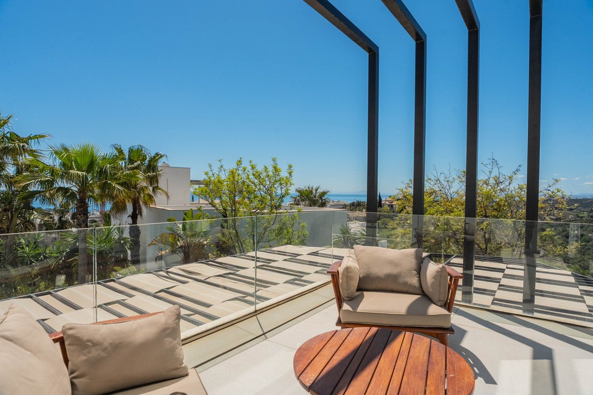 Modern balcony with glass railings, wooden furniture, and panoramic sea view under clear blue sky.