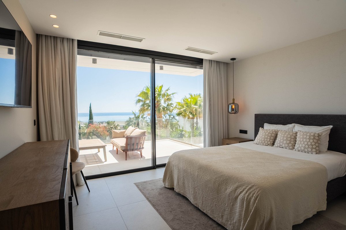 Modern bedroom with ocean view, large glass doors, balcony, and contemporary furnishings.