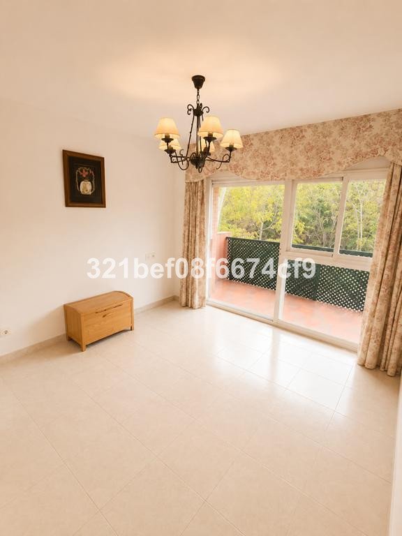 A spacious room with a chandelier and curtains, featuring a balcony with a green railing and trees visible outside.