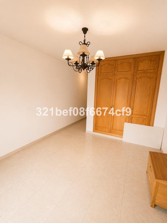 A bedroom with a chandelier, a large wooden wardrobe, and tiled flooring.