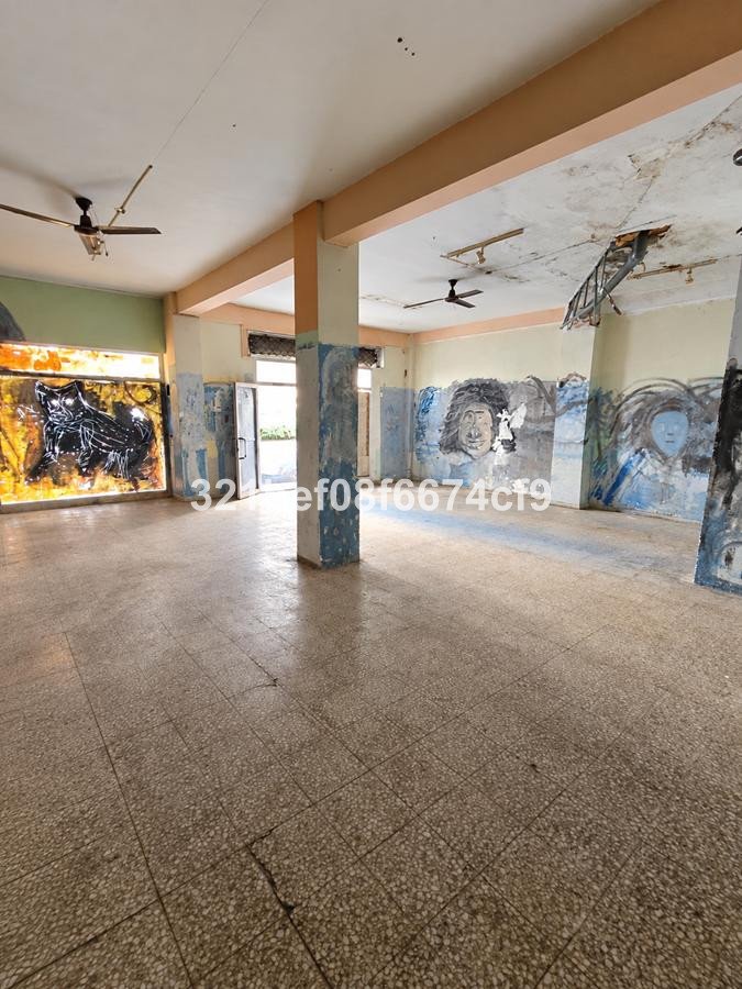 Spacious room with graffiti on walls, tiled floor, and ceiling fans. Appears to be an unfinished or abandoned space.