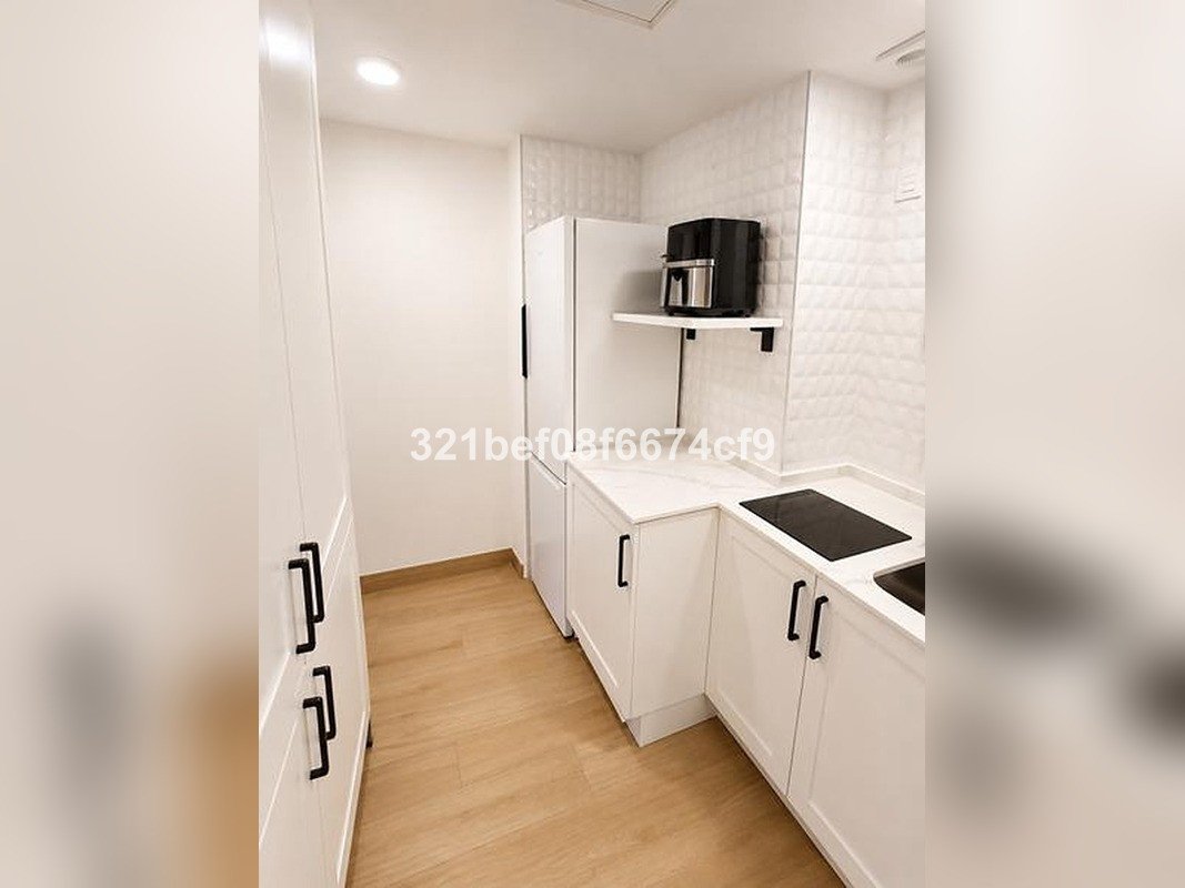 Modern white kitchen with induction hob, built-in refrigerator, and white textured backsplash.