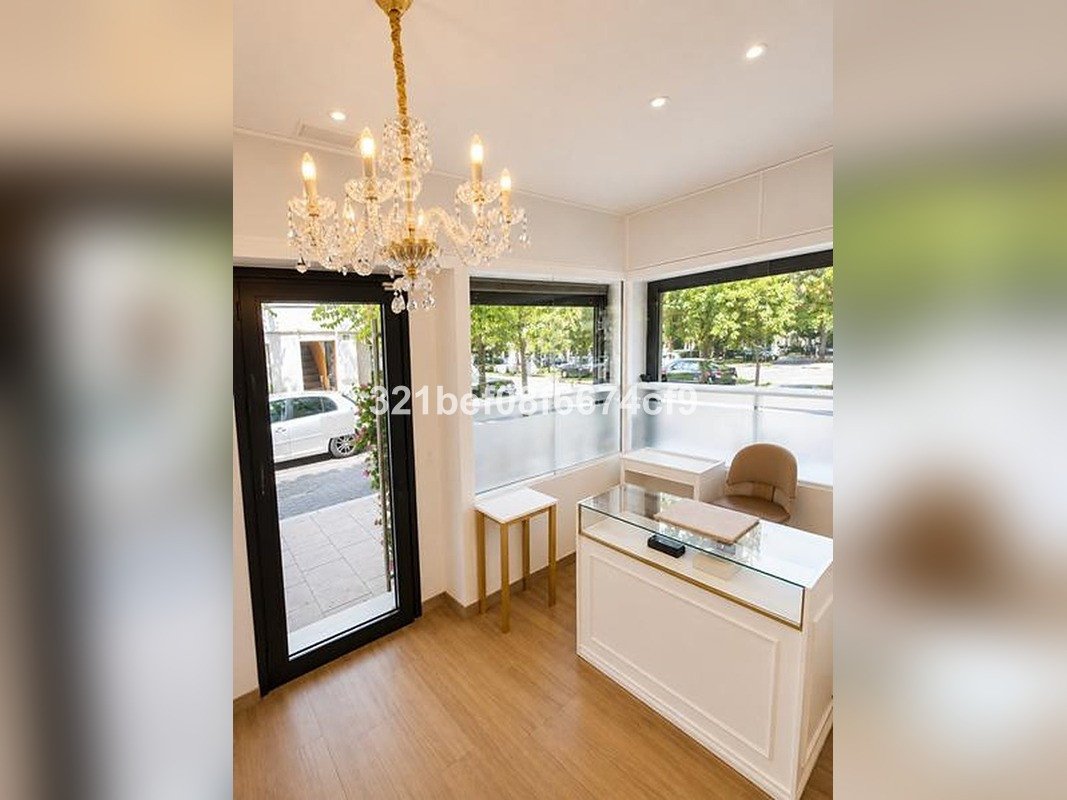 A bright reception area with a glass counter, a chair, a chandelier, and large windows overlooking an outdoor street scene.