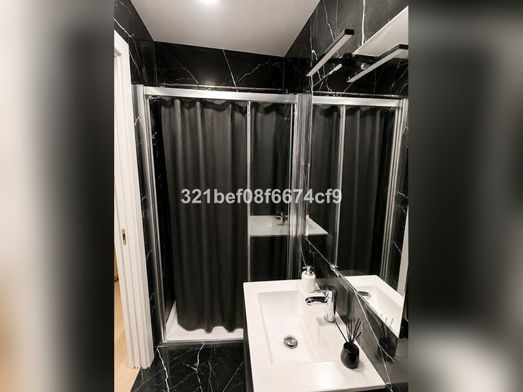 Modern bathroom with black marble walls, a walk-in shower with a black curtain, and a white sink with chrome fixtures.