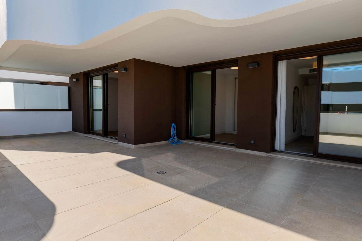 Spacious tiled terrace with dark brown walls and large sliding glass doors offering interior views. Includes a blue hose.