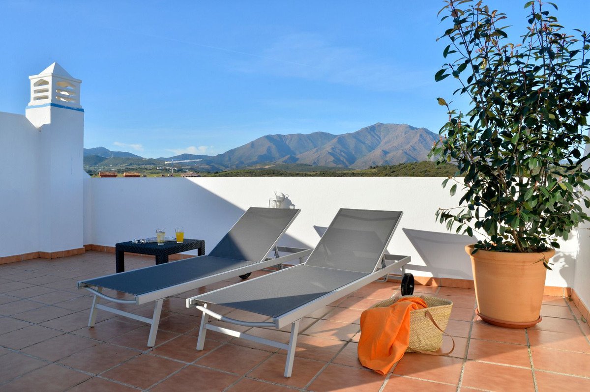 Terrace with sun loungers, drinks, and a plant, offering a scenic mountain view under a clear blue sky.