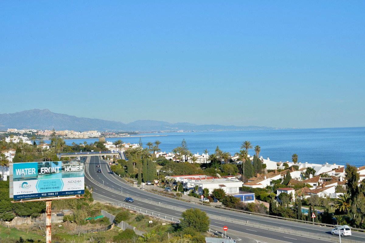 Panoramic view of coastal homes with palm trees, overlooking a highway and the Mediterranean Sea under a clear blue sky.