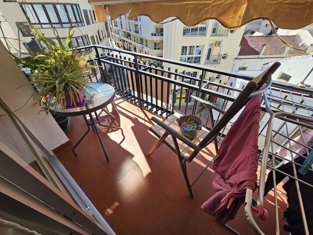 Balcony with table, plant, chair, and clothes drying rack, overlooking urban buildings.