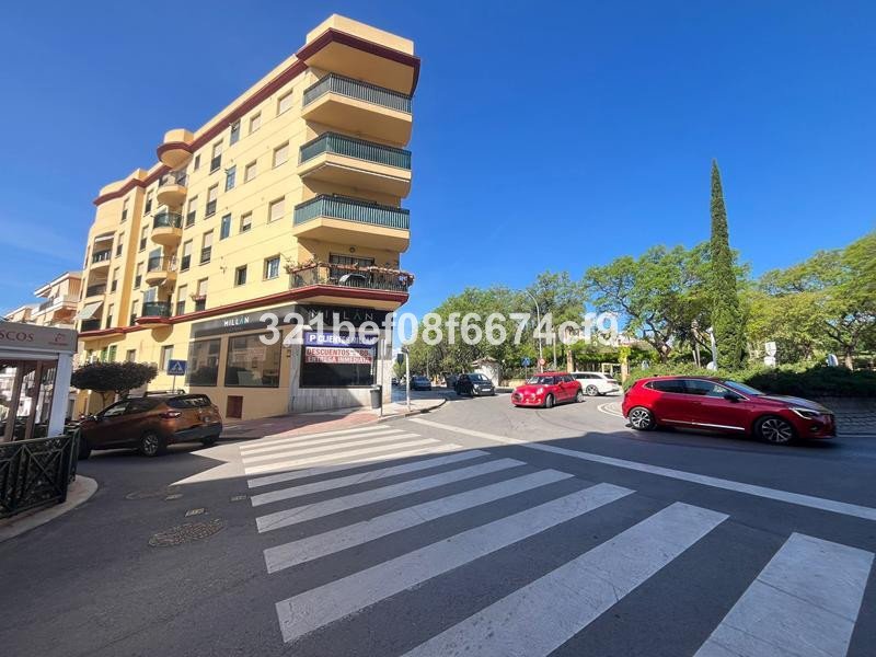 Yellow apartment building with balconies overlooking a street with cars and a crosswalk under a clear blue sky.
