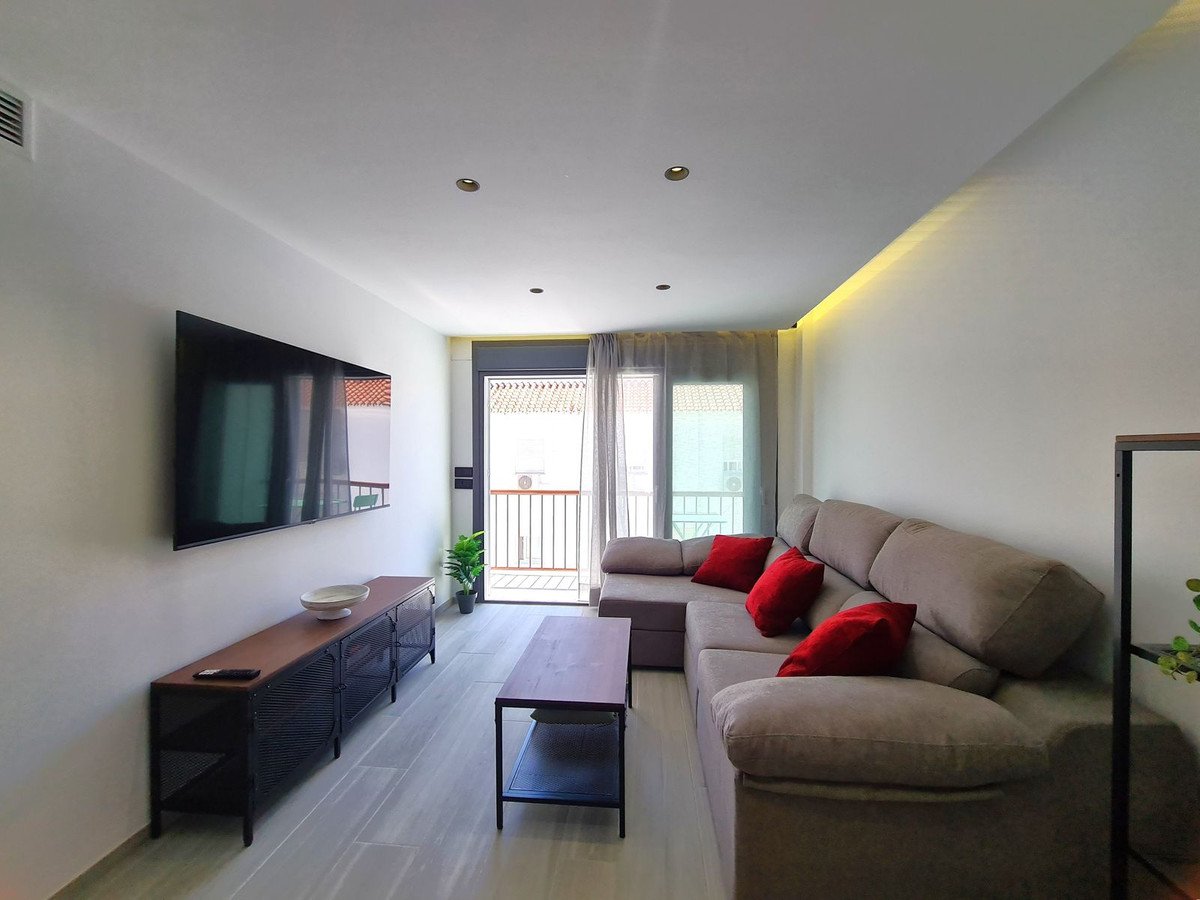 Salón moderno con vista a balcón, sofá beige, TV y muebles de madera.