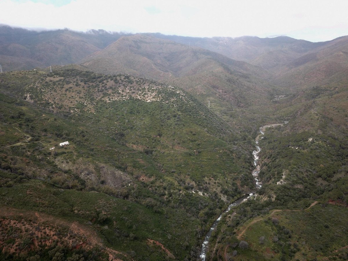 Aerial view of a winding river flowing through a lush, green mountain valley with a house visible on the hillside.