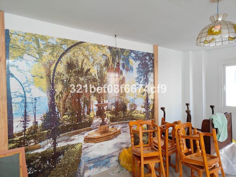 A large tiled mural depicting a scenic garden pathway with a fountain and trees, in a dining area with wooden chairs.