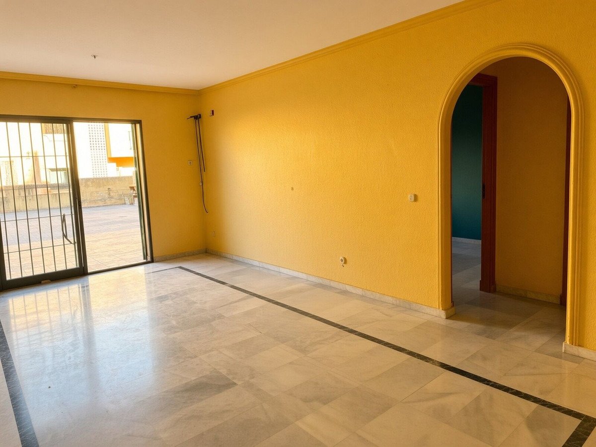 A spacious living room with yellow walls, marble floors, and sliding glass doors leading to a terrace. An arched doorway leads to another room.