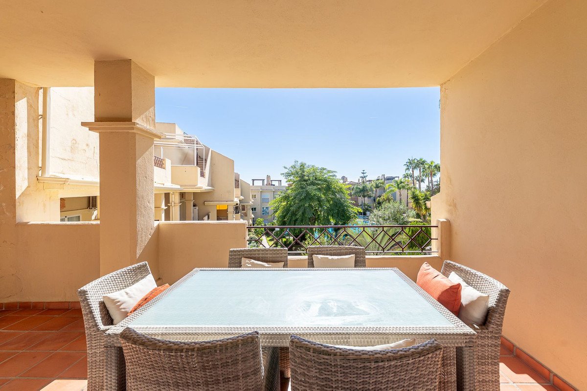 Outdoor patio with dining table and chairs overlooking a pool and buildings