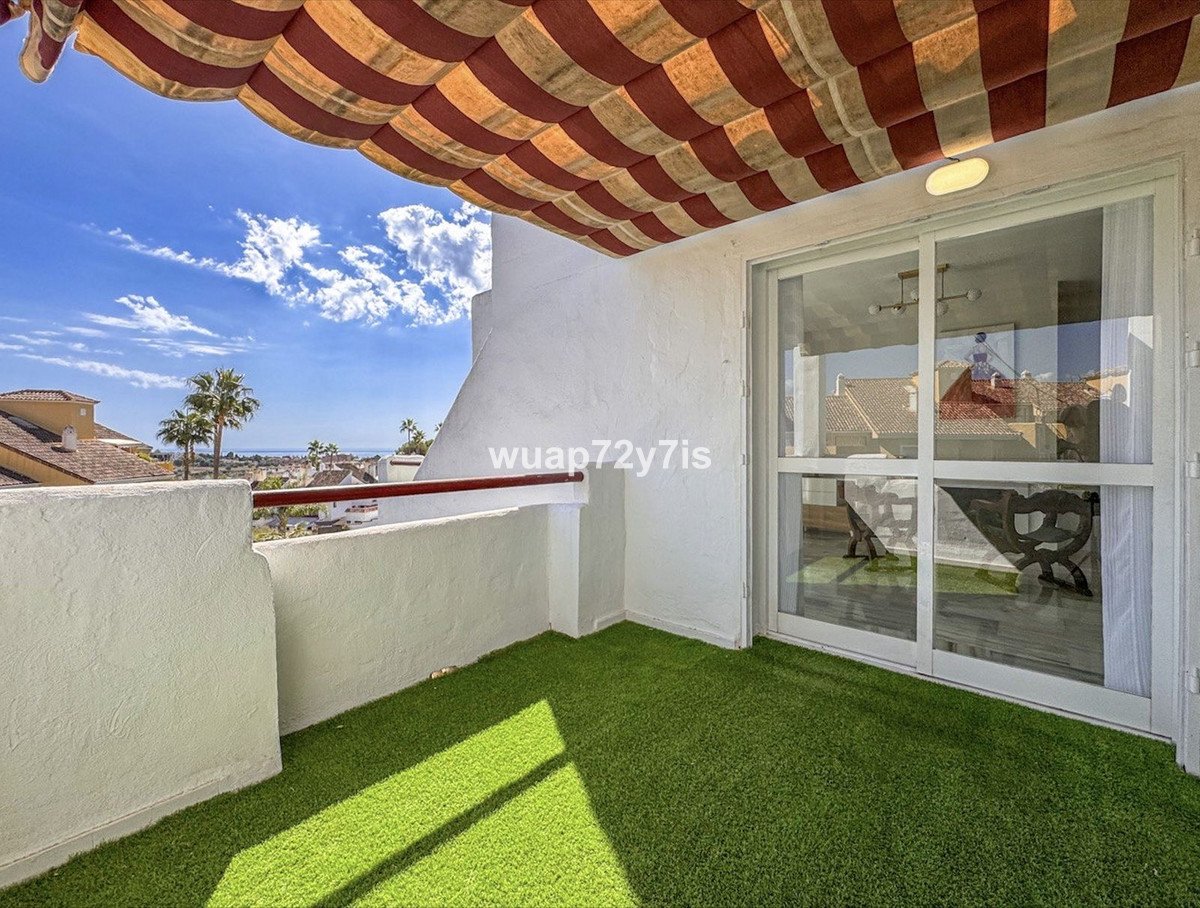 A balcony with artificial grass, sea view, palm trees, and a striped awning overhead.