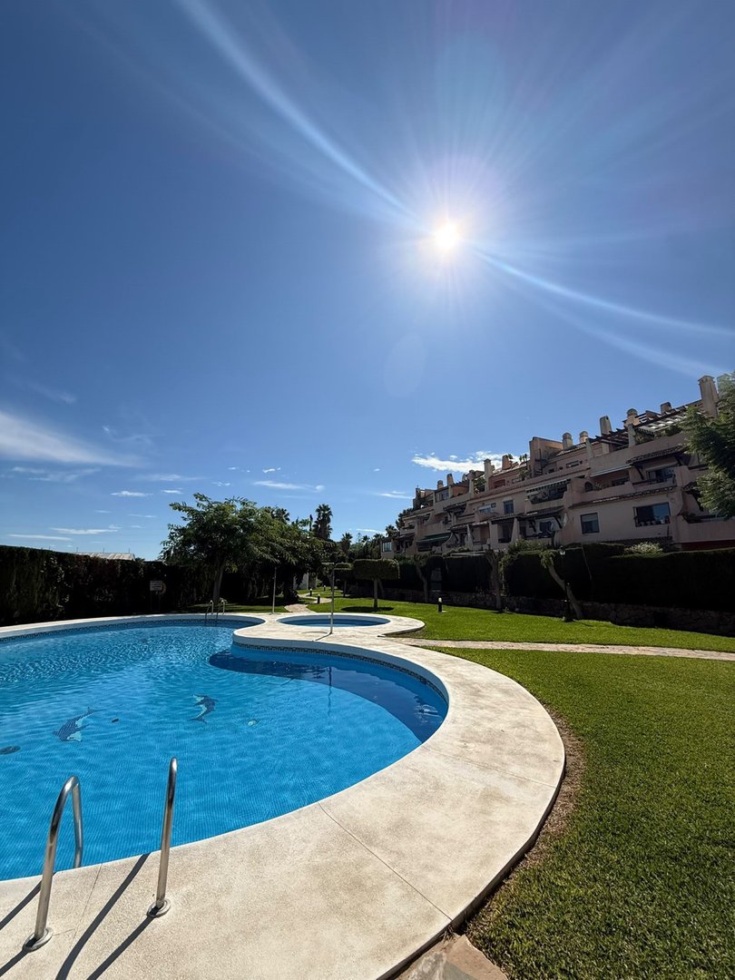A sunny day overlooking a blue swimming pool and a residential complex with green lawns and trees.