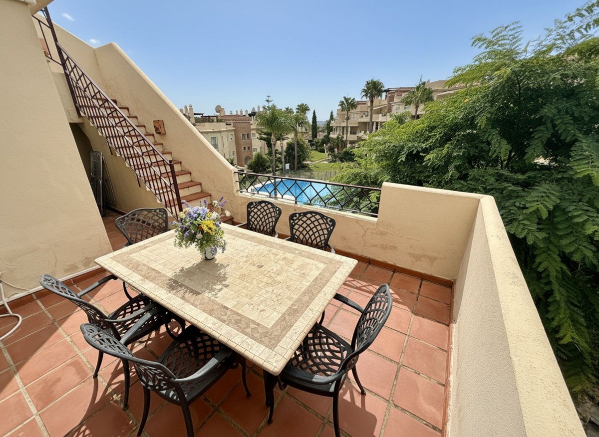 Terrace with outdoor dining table and chairs, overlooking a swimming pool and lush greenery.