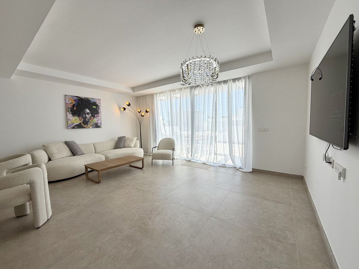 Modern living room with a large sectional sofa, armchair, coffee table, artwork, chandelier, and wall-mounted TV.