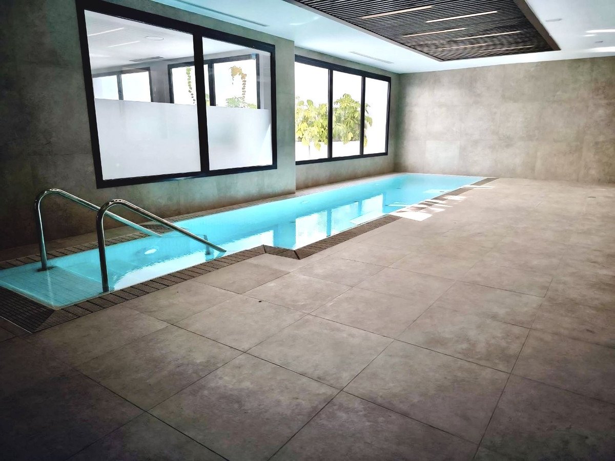 Modern indoor swimming pool with clean blue water, metal handrails, and large windows offering natural light.