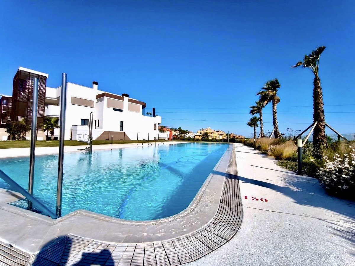 Modern apartment building with swimming pool and palm trees under a clear blue sky.