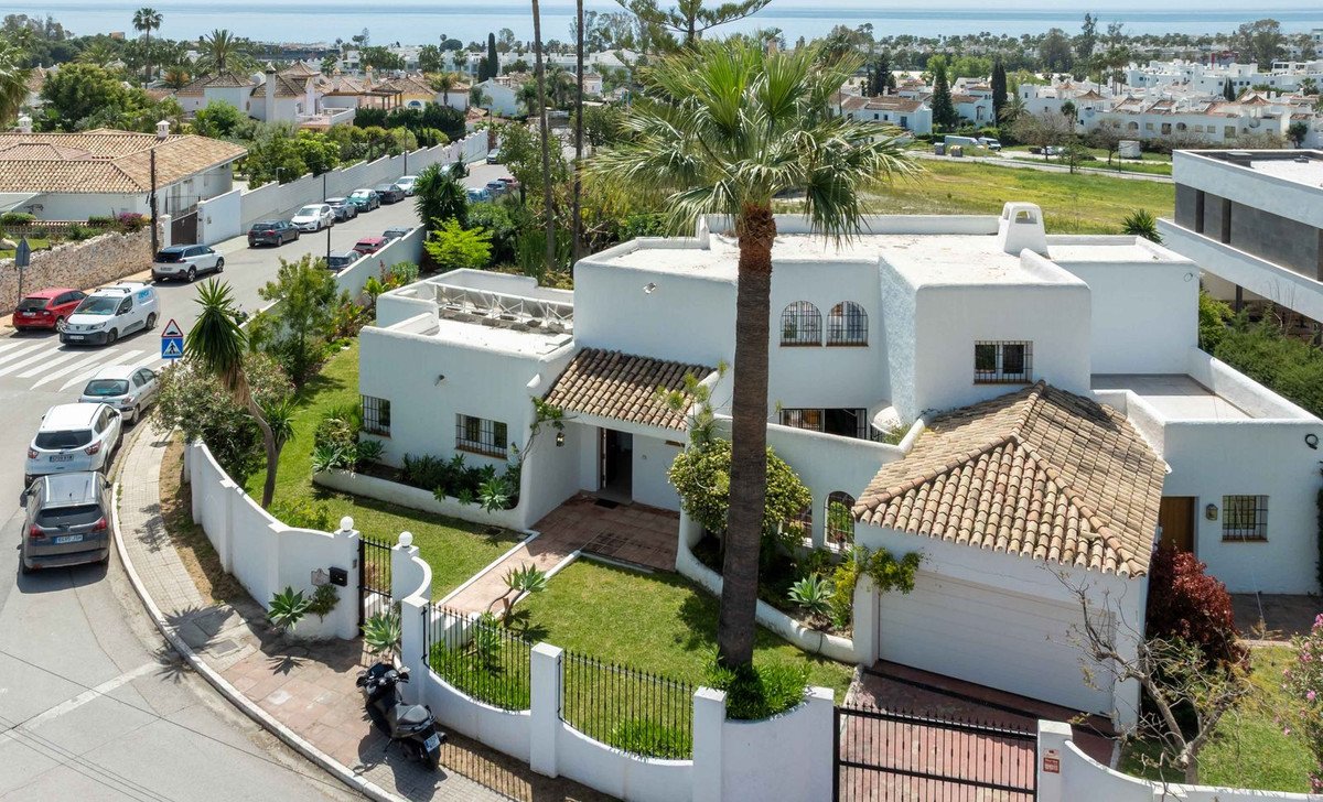 A white villa with a garden, palm trees, and a distant sea view, featuring a garage and private driveway.