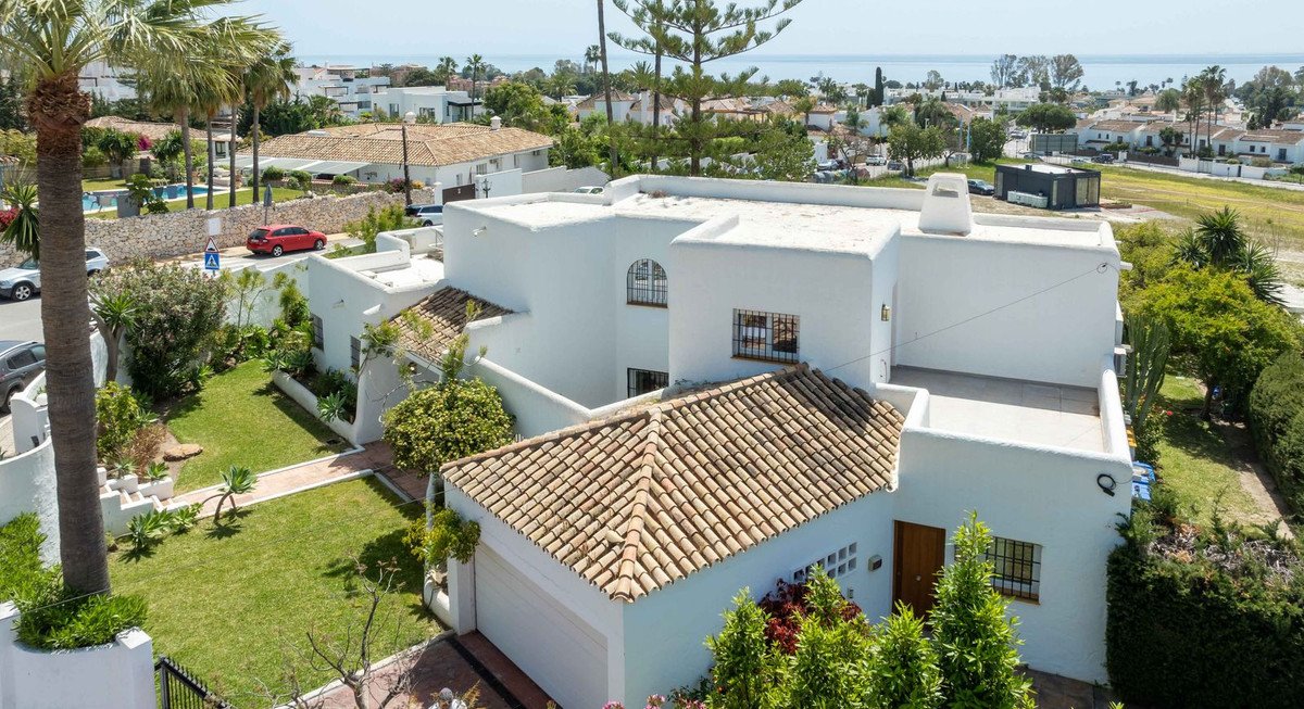 Exterior of a white villa with a terracotta tiled roof, green garden, and a distant view of the sea.