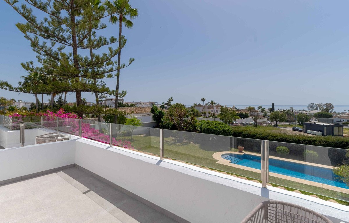 A private balcony with a swimming pool and sea view, surrounded by palm trees and lush greenery.