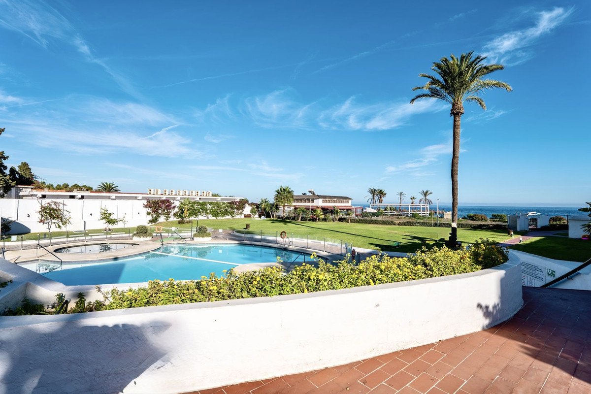 A swimming pool and hot tub area with a view of the sea and palm trees under a clear blue sky.