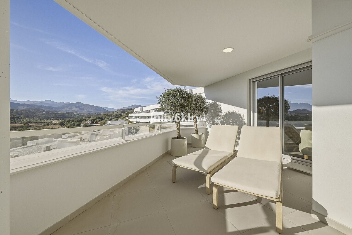 A spacious balcony with two lounge chairs and potted trees, offering a beautiful mountain view under a clear blue sky.
