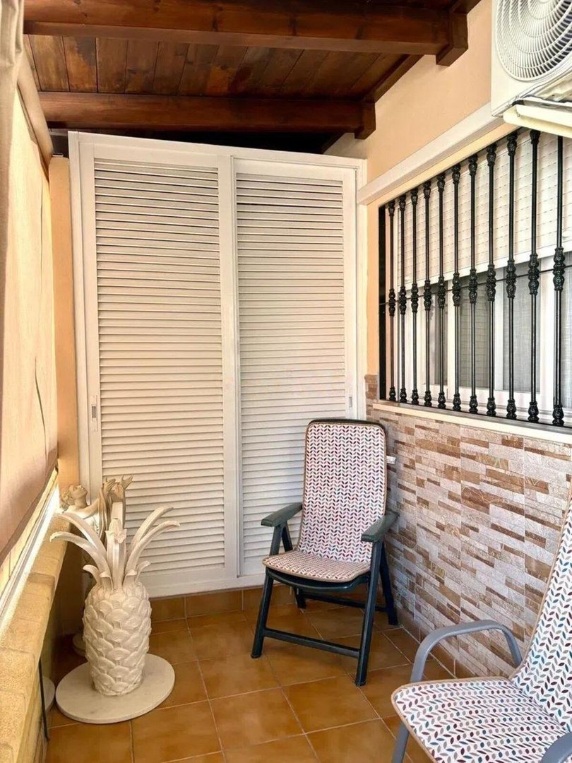 A balcony with two chairs, decorative pineapple statue, and white sliding doors with louvered panels.