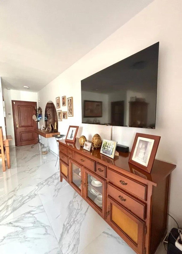 A modern living room featuring a large flat-screen TV mounted above a wooden buffet with decorative items and framed photos.