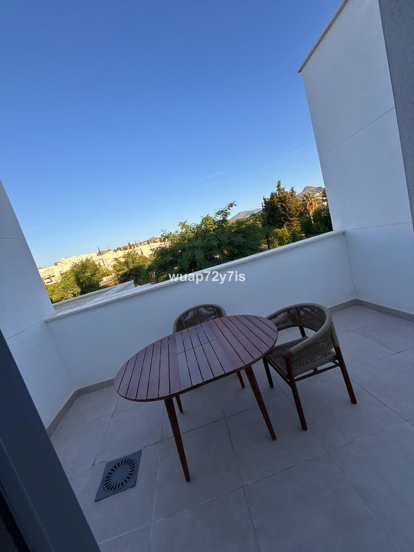 Balcony with wooden table and chairs overlooking greenery and distant buildings