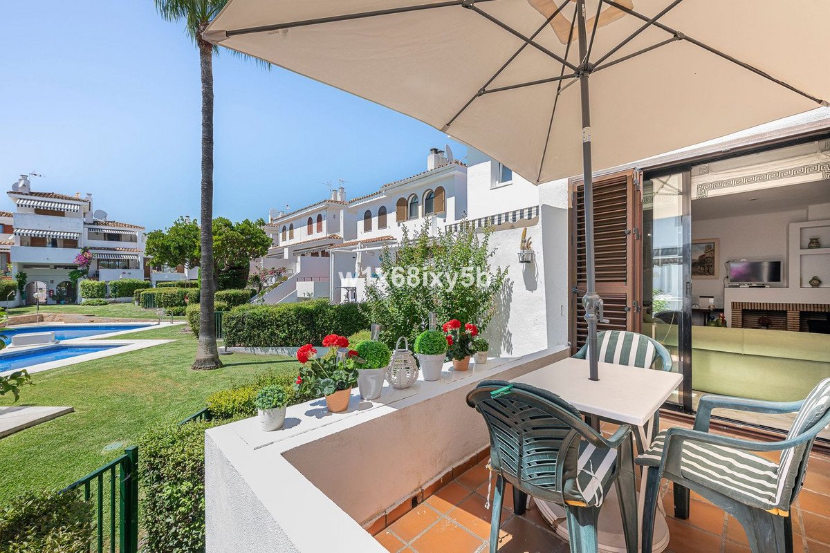 Outdoor terrace with patio furniture, umbrella, and view of swimming pool and surrounding buildings