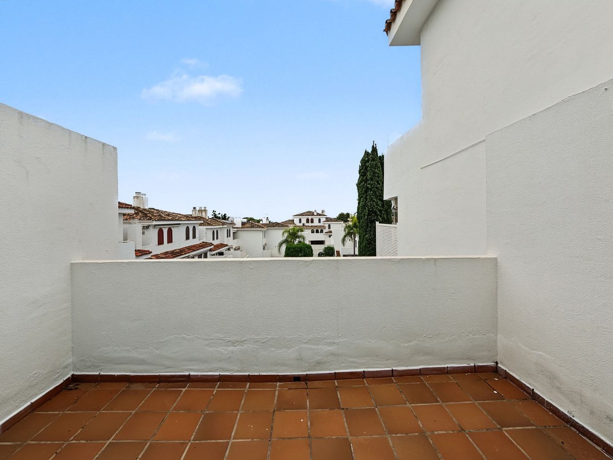 Tiled terrace with a view of white buildings, red tile roofs, palm trees, and a blue sky.