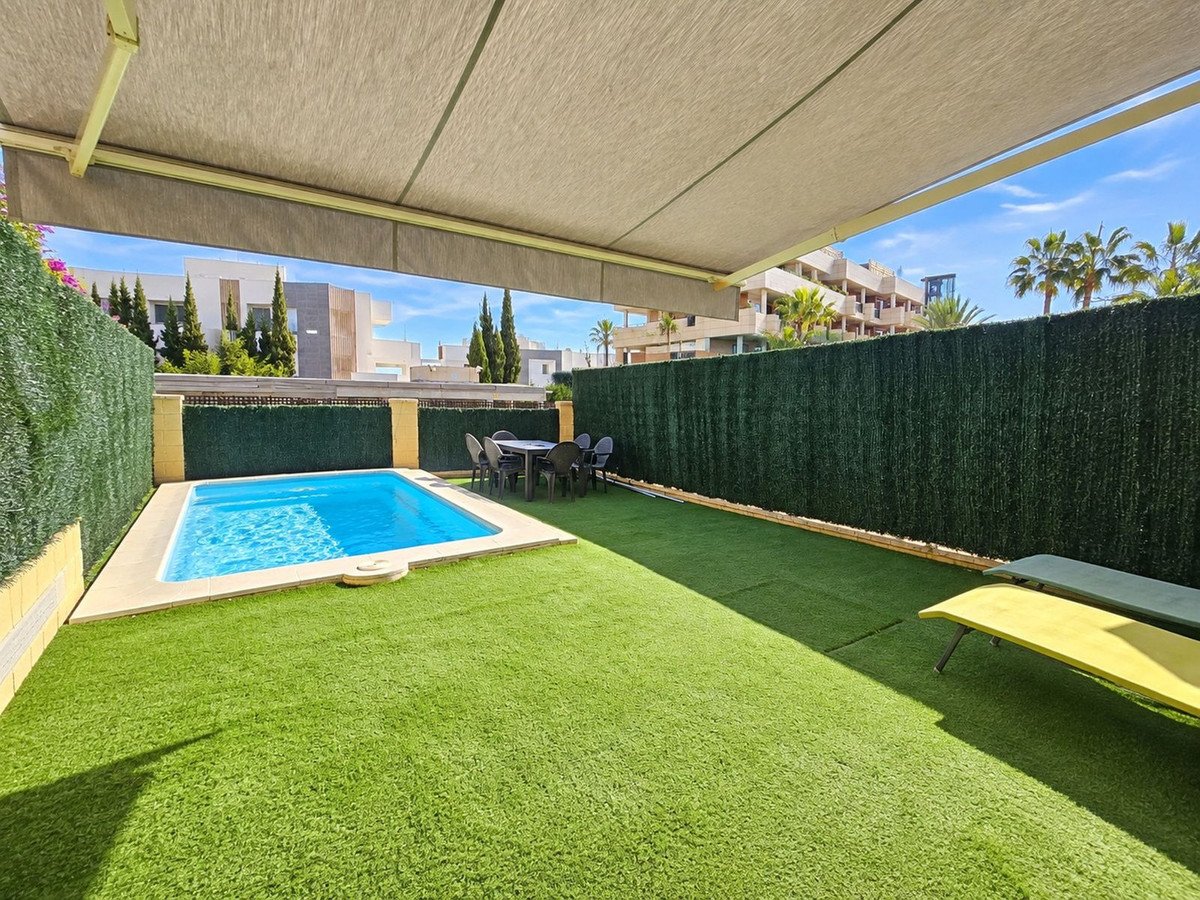 Private outdoor terrace with a small swimming pool, dining table, sunbeds, and artificial grass. Features a retractable awning overhead.