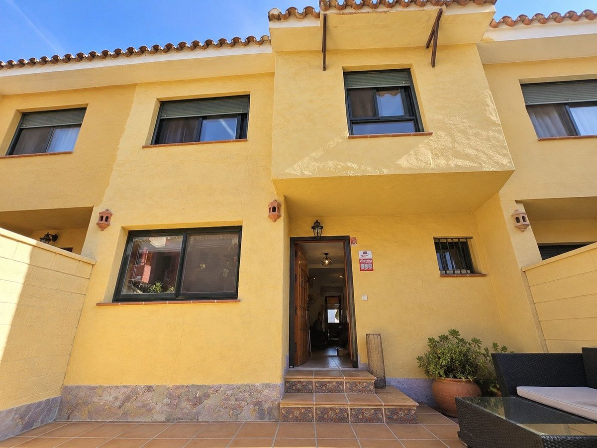 Yellow townhouse exterior with entrance, windows, and a tiled terrace with outdoor seating and plants.
