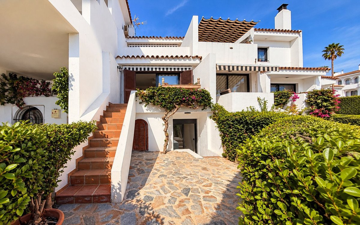Terrace with stairs, lush garden, and sunny blue sky. White building with awnings.