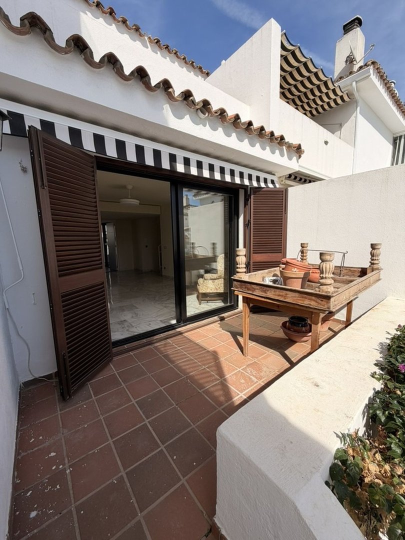 Terrace with sliding doors leading to an interior living space, featuring awnings and a wooden table with potted plants.