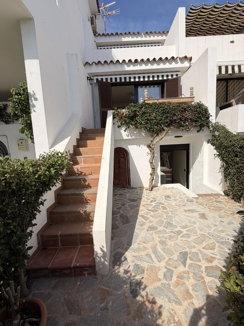 Exterior view of a house with a stone pathway leading to stairs and an entryway, surrounded by greenery.