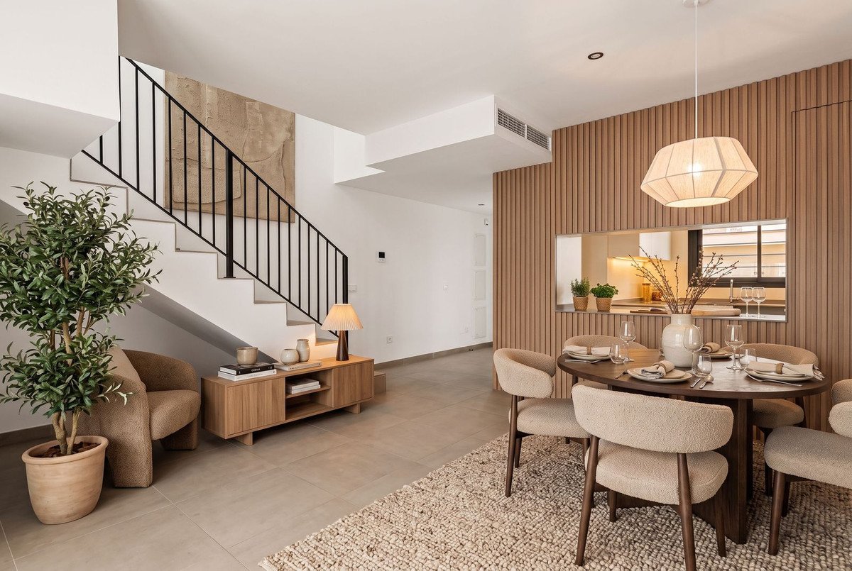 Modern dining area with chairs around table, next to living space with stairs and a plant.