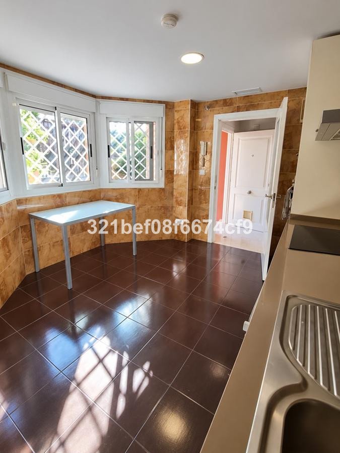 A corner kitchen with tiled walls, a dining table near the window, and a view of greenery outside.