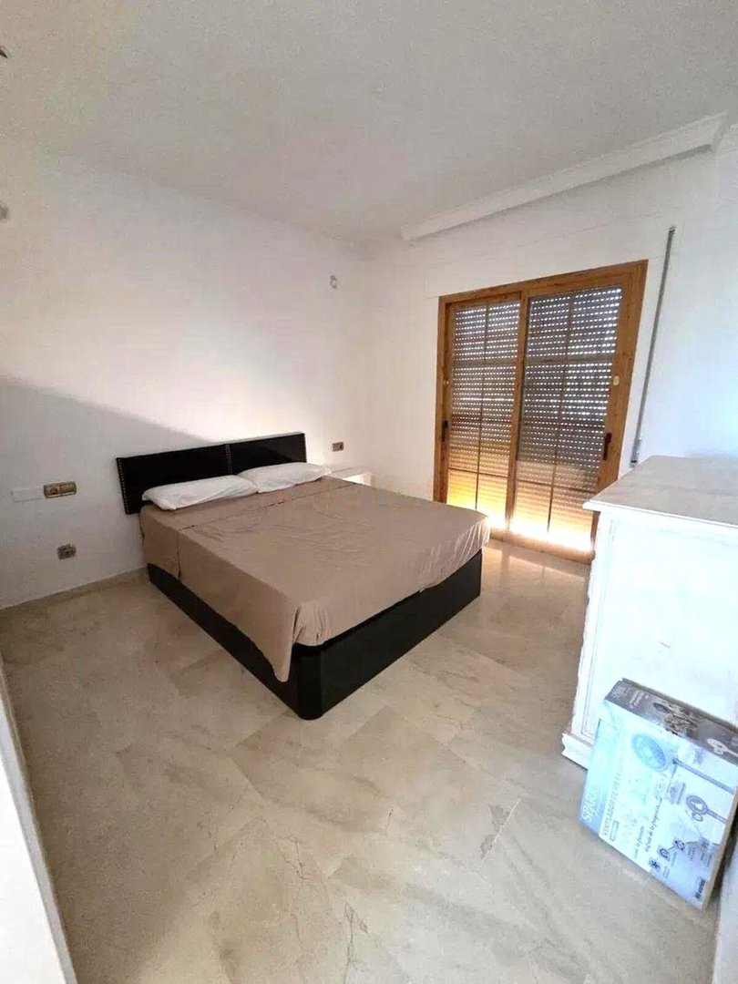 Bedroom with a large bed, marble floors, and a sliding glass door leading outside.