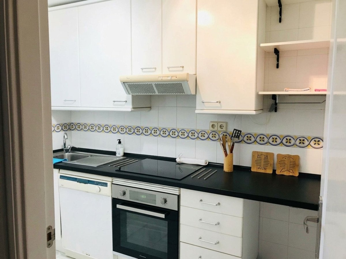 A modern kitchen with white cabinets, black countertops, sink, dishwasher, and oven.