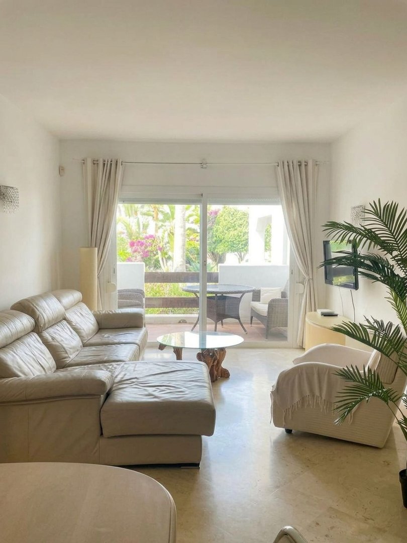 Modern living room with a large sectional sofa, armchair, coffee table, and a view of a balcony with outdoor seating.