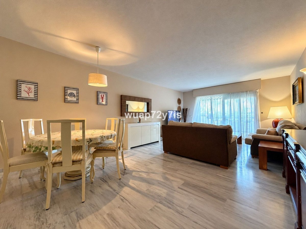 A bright and spacious living and dining area with comfortable seating and a large window with sheer curtains.