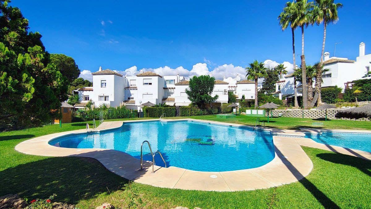 A large blue swimming pool with steps and surrounding grass, with white buildings and palm trees in the background under a clear blue sky.