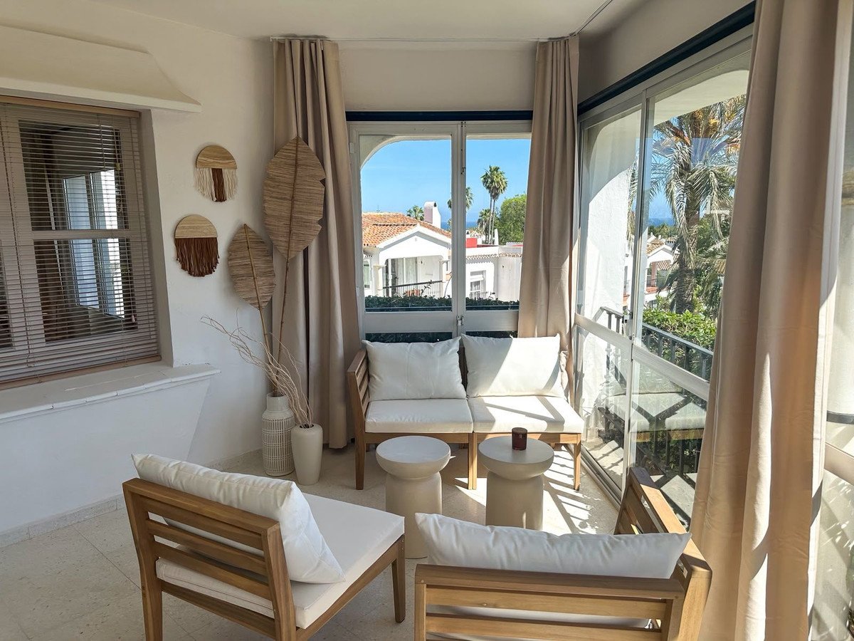 Comfortable balcony seating area with white cushions, offering a beautiful view of palm trees and coastal houses.
