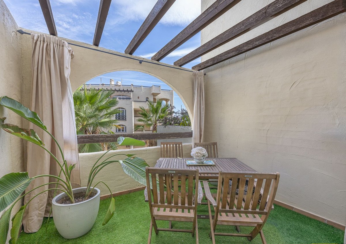 Covered terrace with wooden dining set, artificial grass, and views of palm trees and buildings.